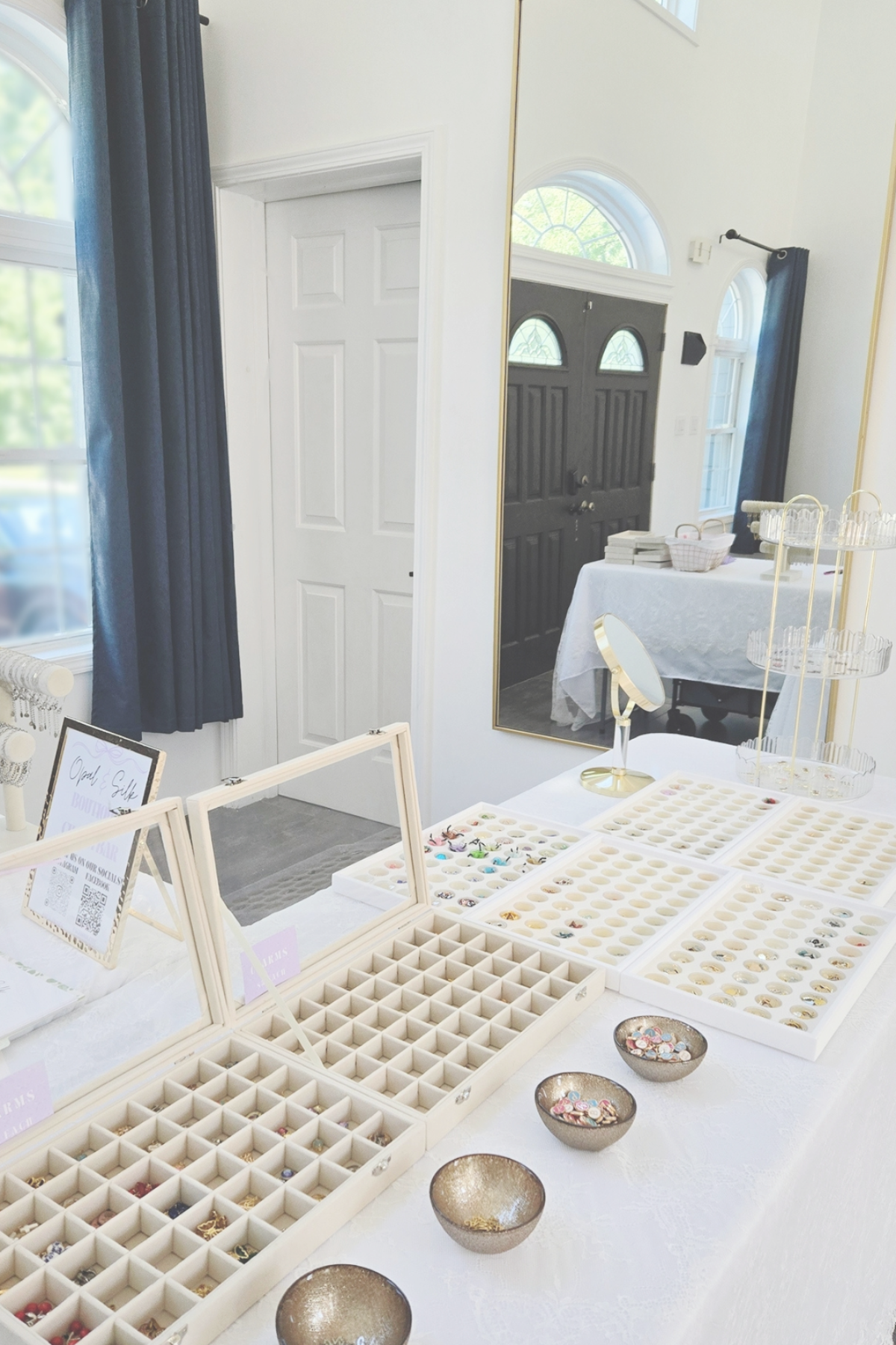 Jewelry display setup with trays and small bowls on a table in a room with large windows.